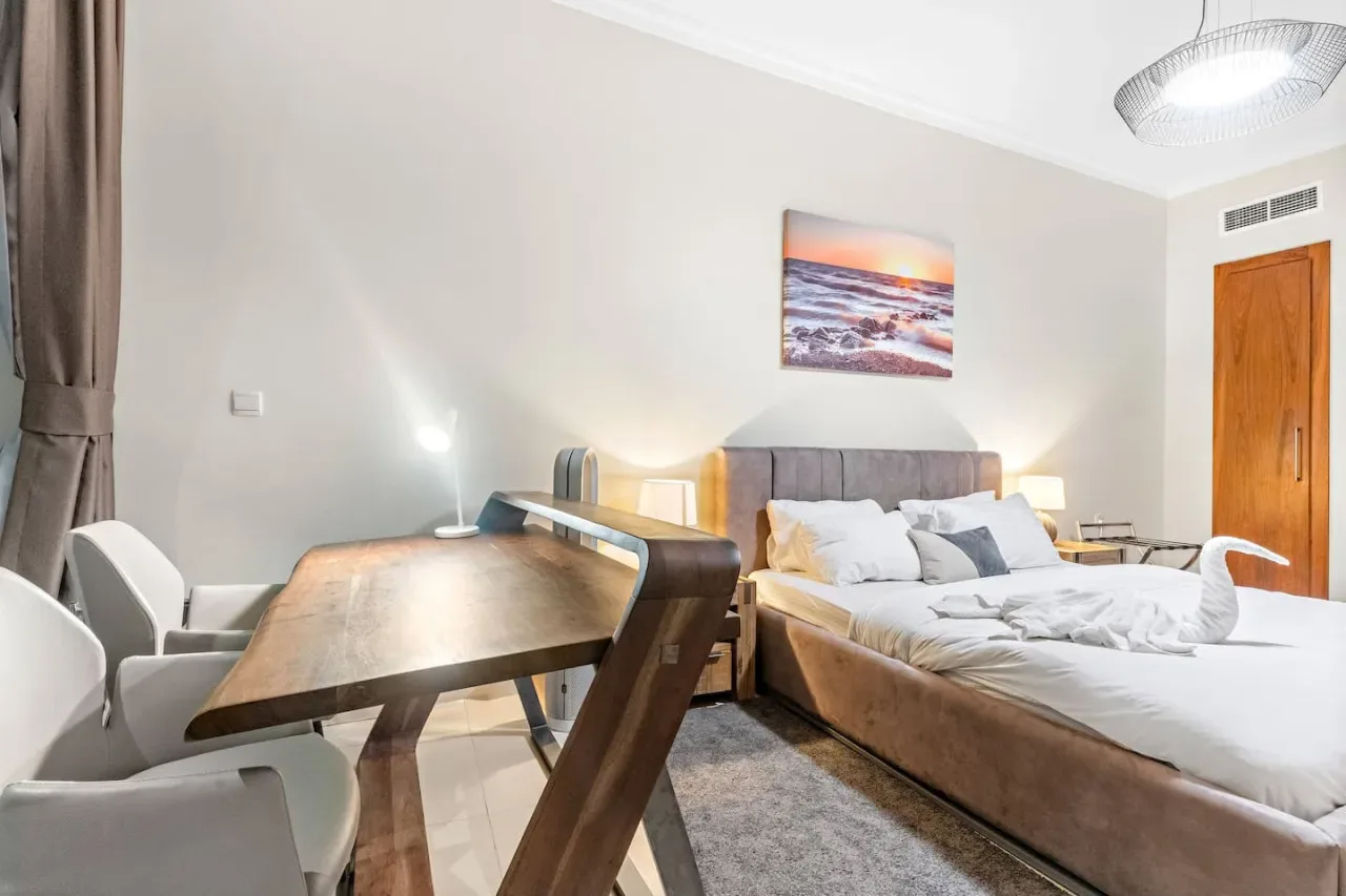 Un dormitorio con una cama, un escritorio y sillas junto a una ventana con cortinas.