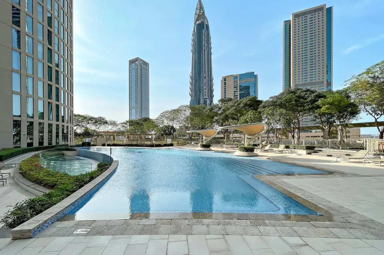 Una piscina está rodeada de edificios altos y vegetación ajardinada.