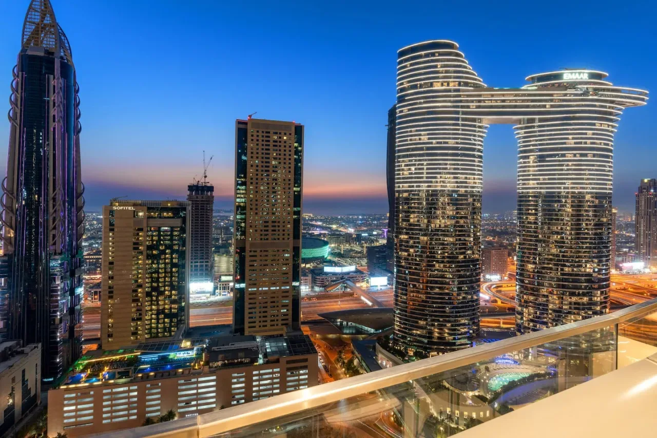 Panorámica urbana al anochecer, con edificios altos iluminados y vías.