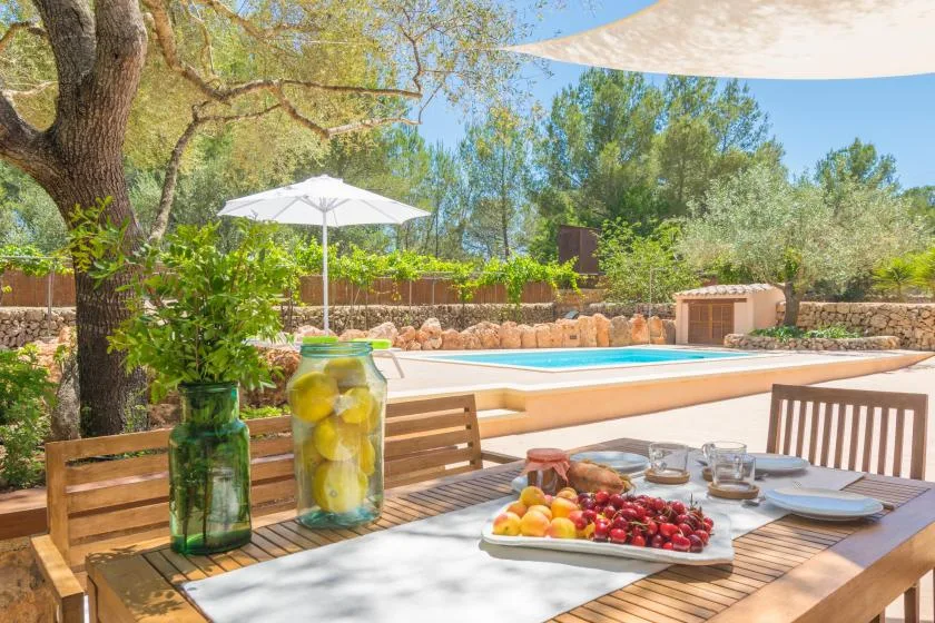 Una mesa de comedor al aire libre junto a una piscina, con fruta dispuesta sobre la mesa.