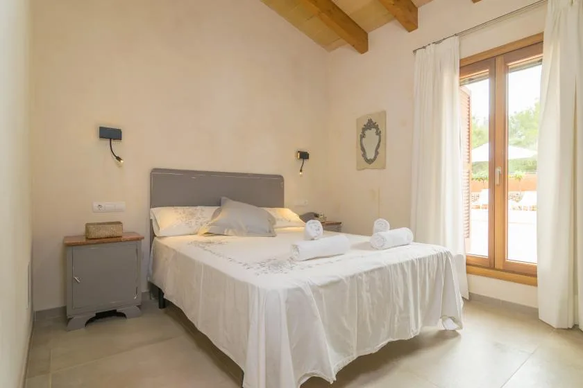 Un dormitorio luminoso con una cama bien tendida y puertas de vidrio que dan a un patio.