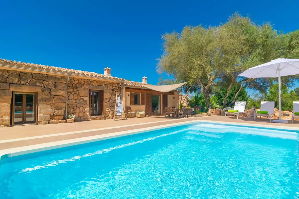 Una piscina exterior junto a una casa de piedra, con asientos a la sombra.
