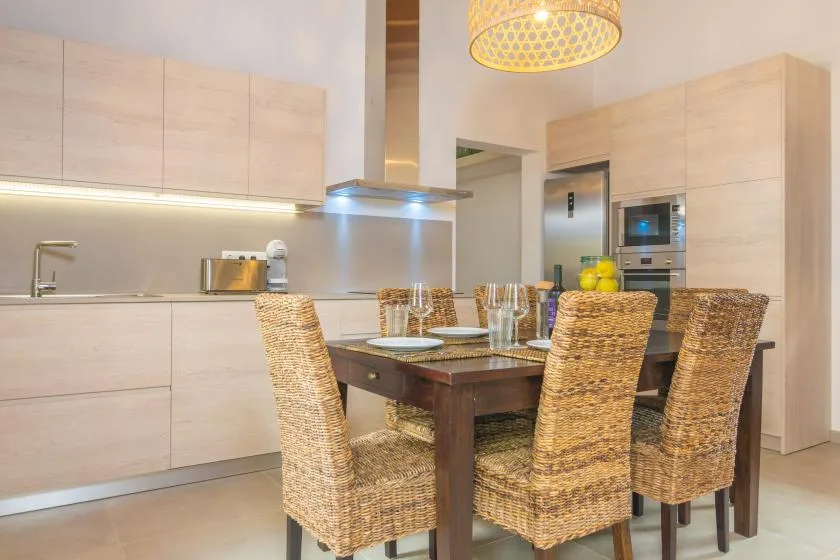 Un comedor con asientos tejidos y una mesa de madera junto a una cocina moderna.