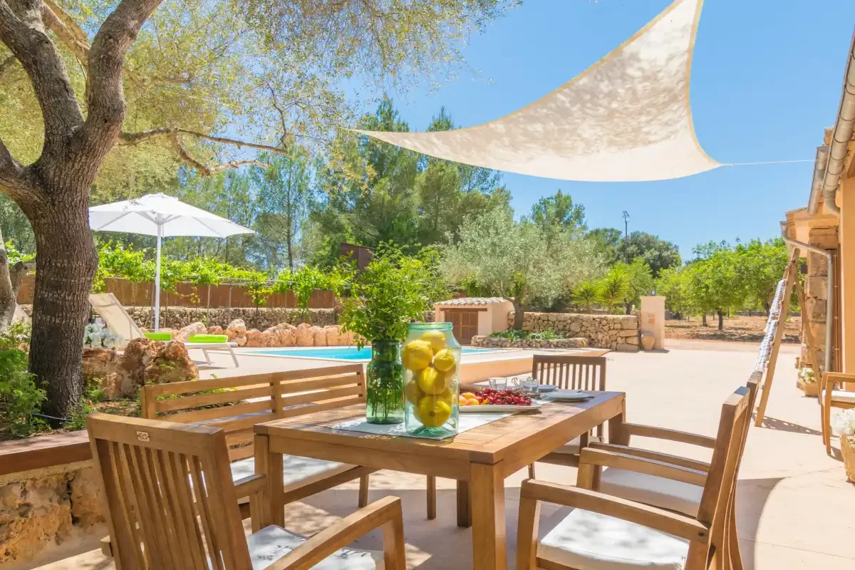 Un patio comedor al aire libre con asientos de madera bajo una vela de sombra.