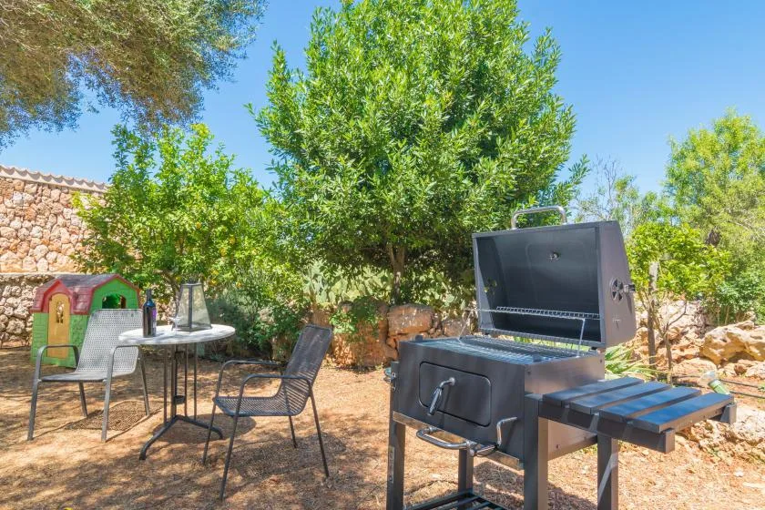 Un patio ajardinado con una parrilla, asientos al aire libre y árboles frondosos.