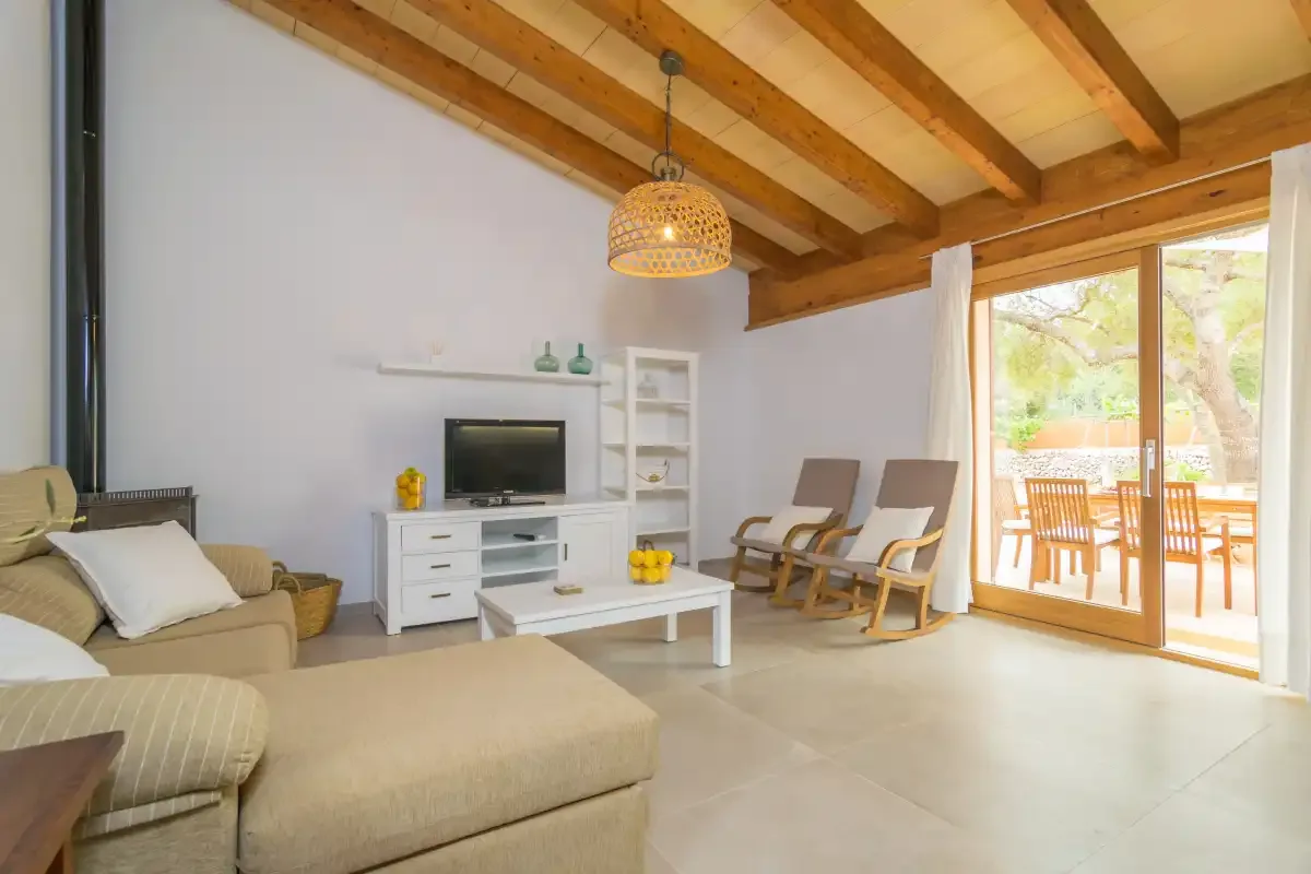 Una sala de estar luminosa con asientos, un televisor y grandes puertas de vidrio que dan a un patio.