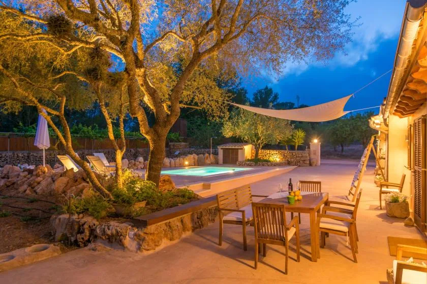 Un patio al aire libre con una mesa de comedor junto a una piscina iluminada.