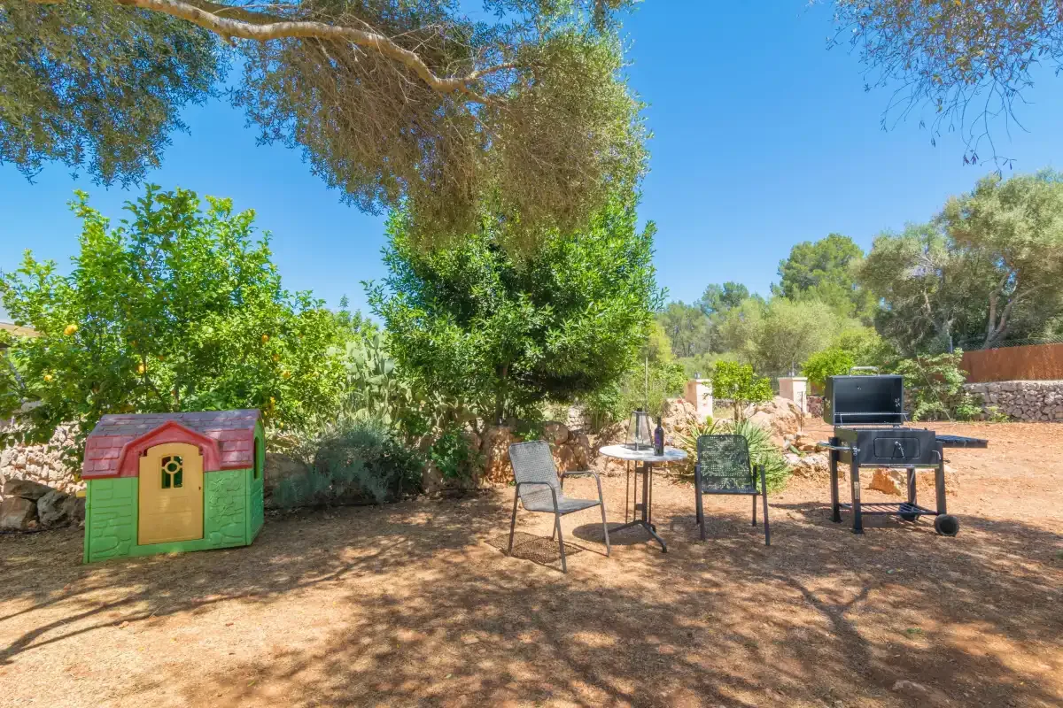 Una zona exterior de estar a la sombra con una casita de juegos y una barbacoa.