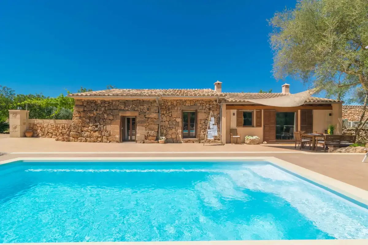 Una casa de piedra y un patio sombreado dan a una piscina.