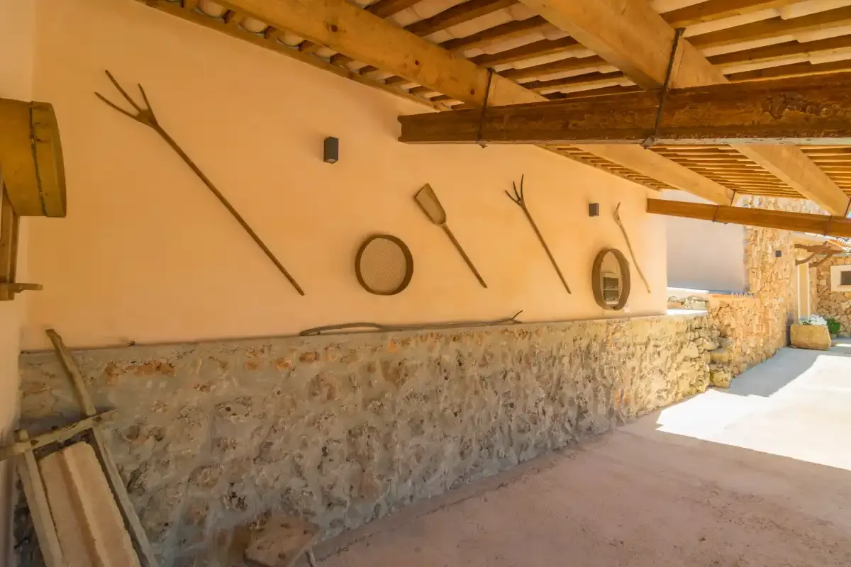 Un pasillo cubierto de estilo rústico tiene paredes inferiores de piedra y vigas de madera.