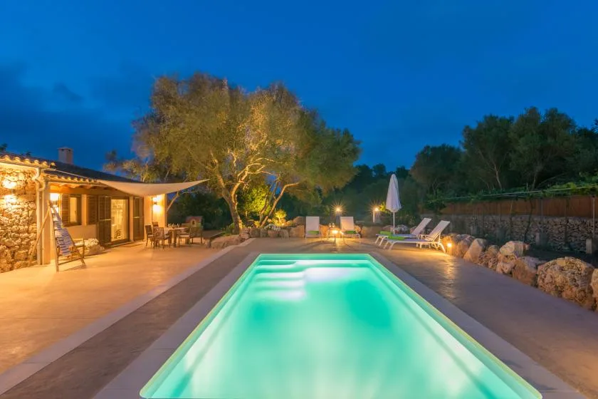 Una piscina iluminada está junto a un patio exterior al anochecer.