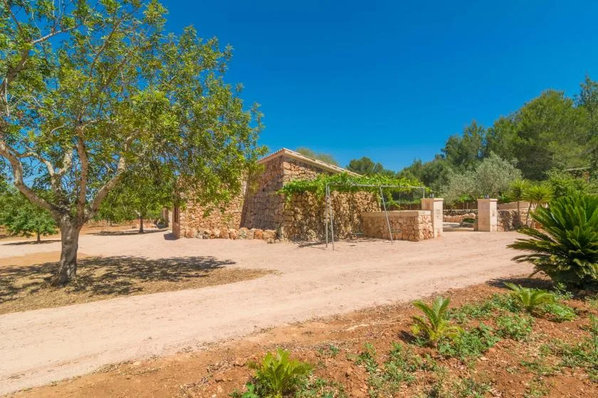 Un edificio de piedra está junto a un camino de tierra, rodeado de árboles y arbustos.
