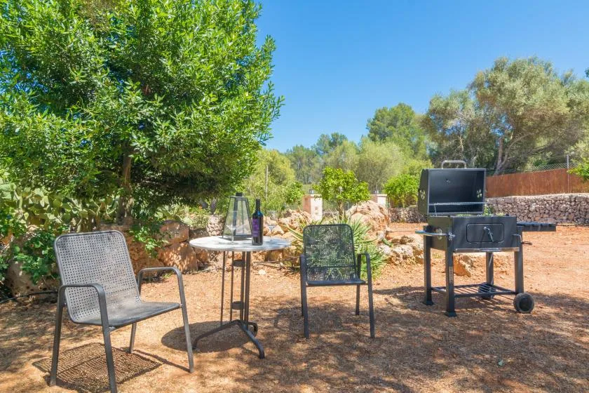 Una zona de estar al aire libre con una mesa y una parrilla entre árboles.