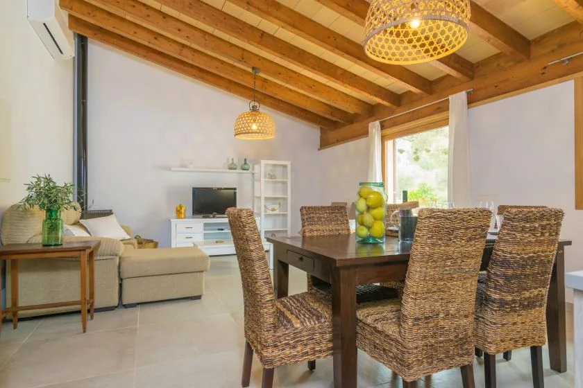 Una luminosa sala de estar y comedor con una mesa de madera y asientos tejidos bajo vigas vistas.