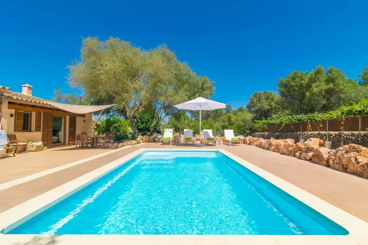 Una piscina al aire libre junto a un patio con asientos y una sombrilla.
