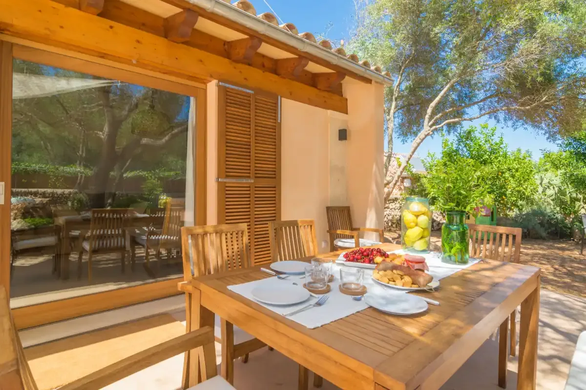 Comedor exterior con una mesa de madera preparada con platos y comida.