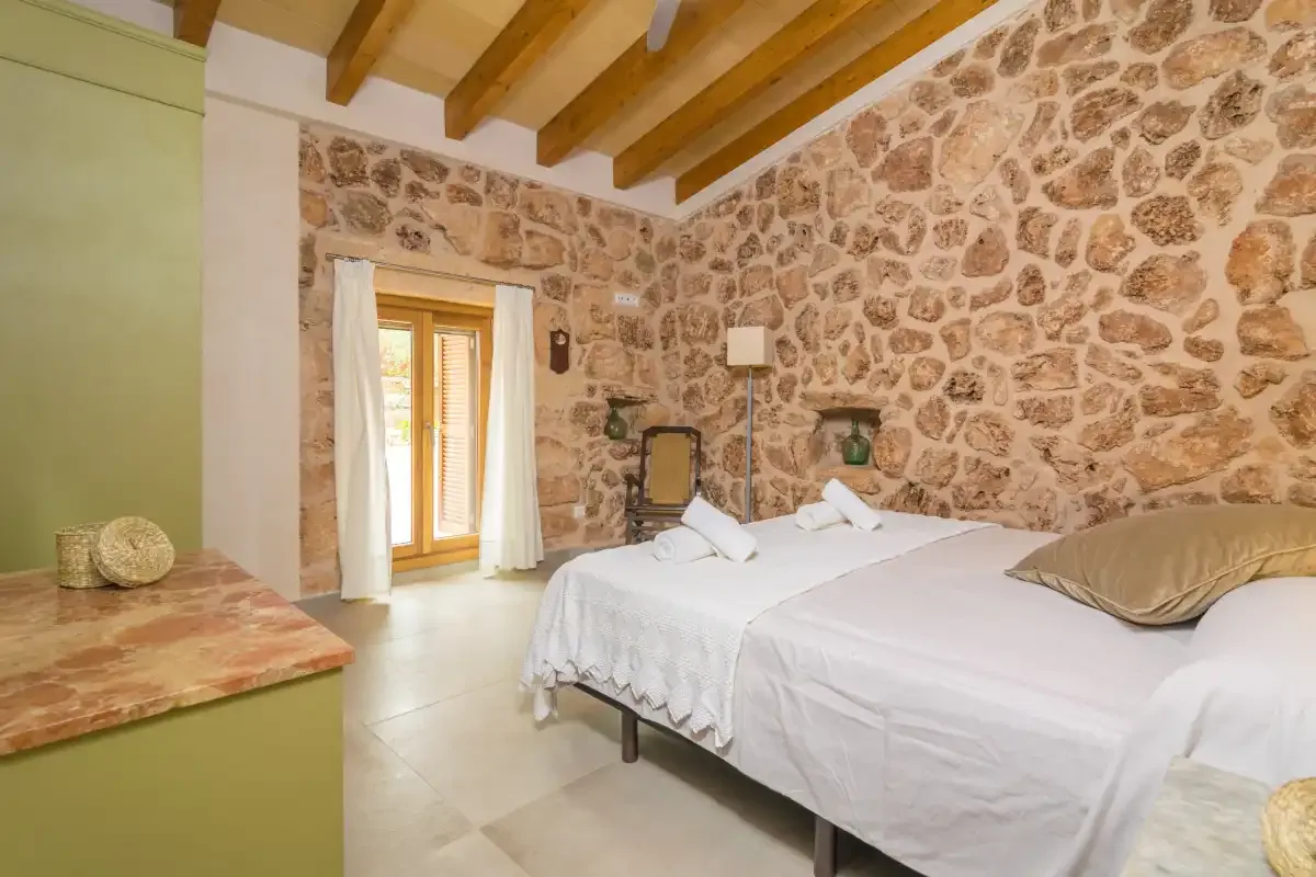 Un dormitorio con ropa de cama blanca, vigas expuestas y una pared de piedra.