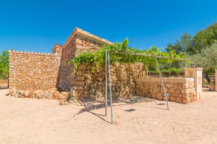 Un edificio rústico de piedra está junto a una zona exterior arenosa con una estructura metálica.