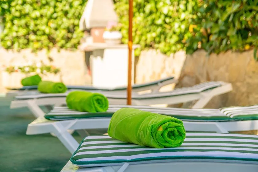 Poolside seating with green towels rests beside the water.