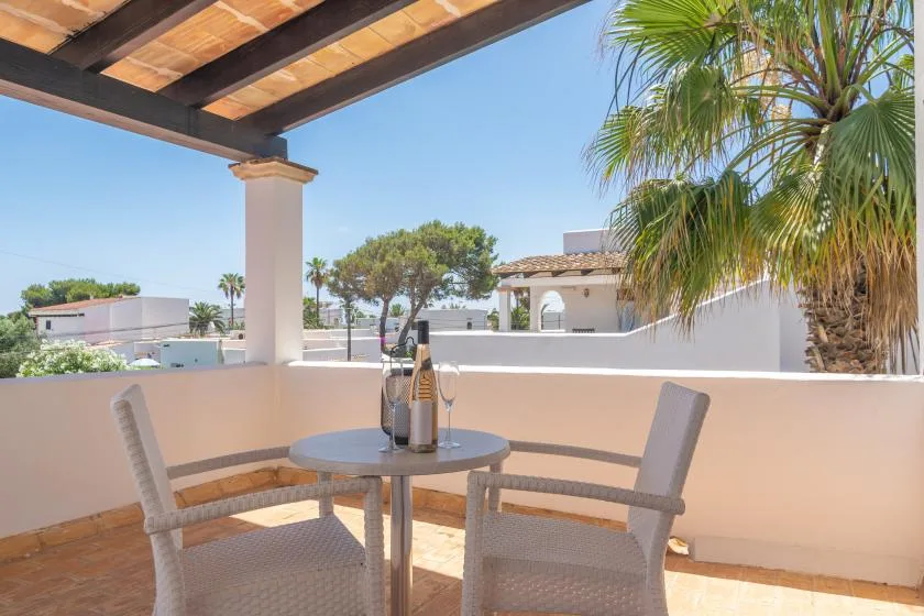 A shaded outdoor terrace with a round table and seating overlooking nearby buildings and palm trees.