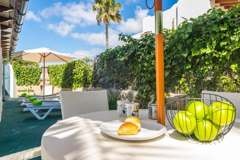 An outdoor patio with shaded seating, greenery, and a table set with fruit and pastries.