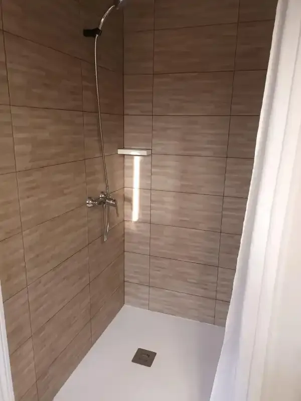 A tiled shower with a handheld showerhead and white curtain.