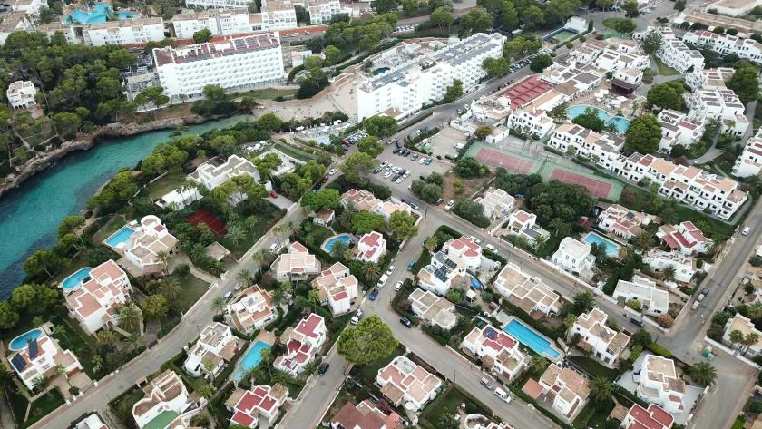 An aerial view of a residential neighborhood with white buildings, roads, and a turquoise waterway.