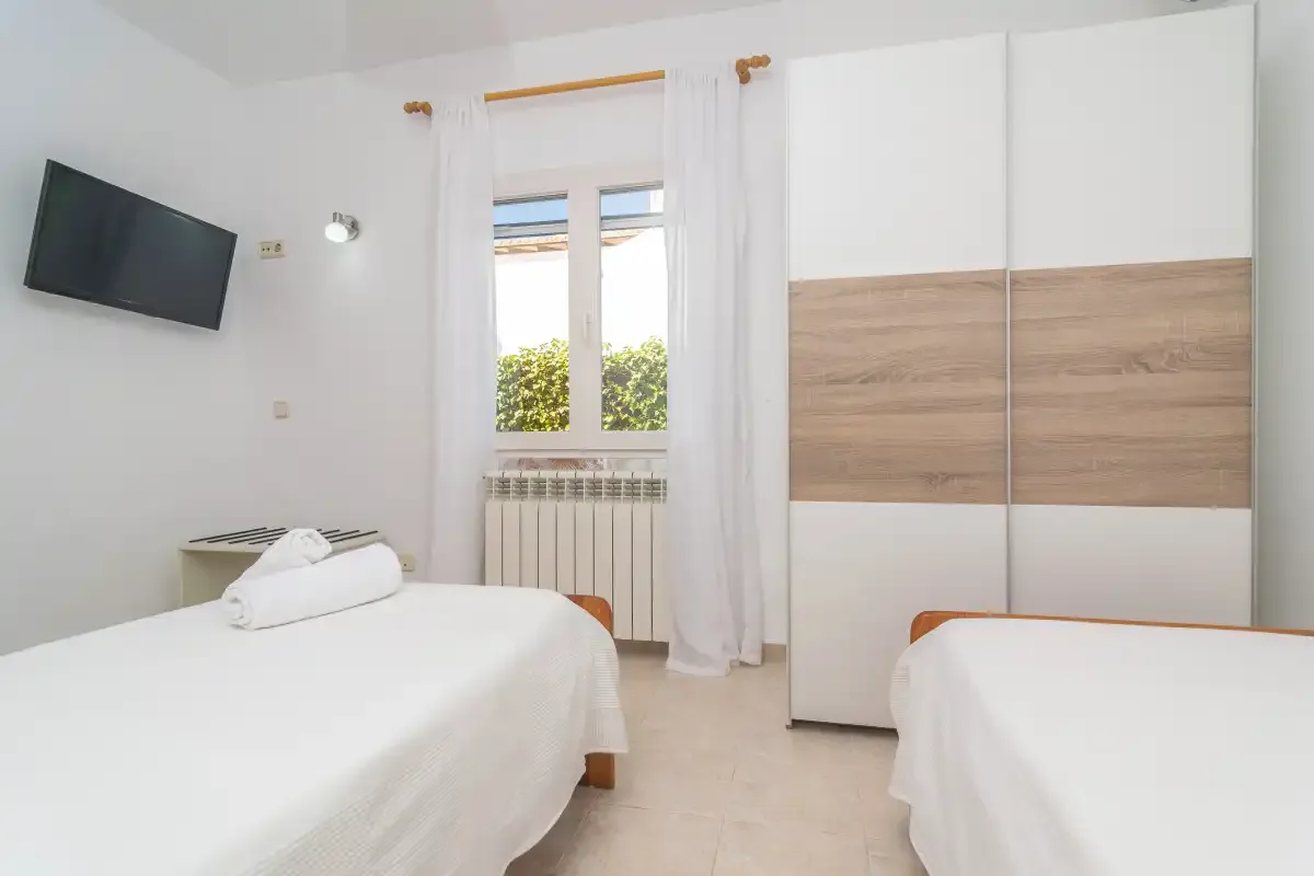 A bright bedroom with two beds and a wardrobe.
