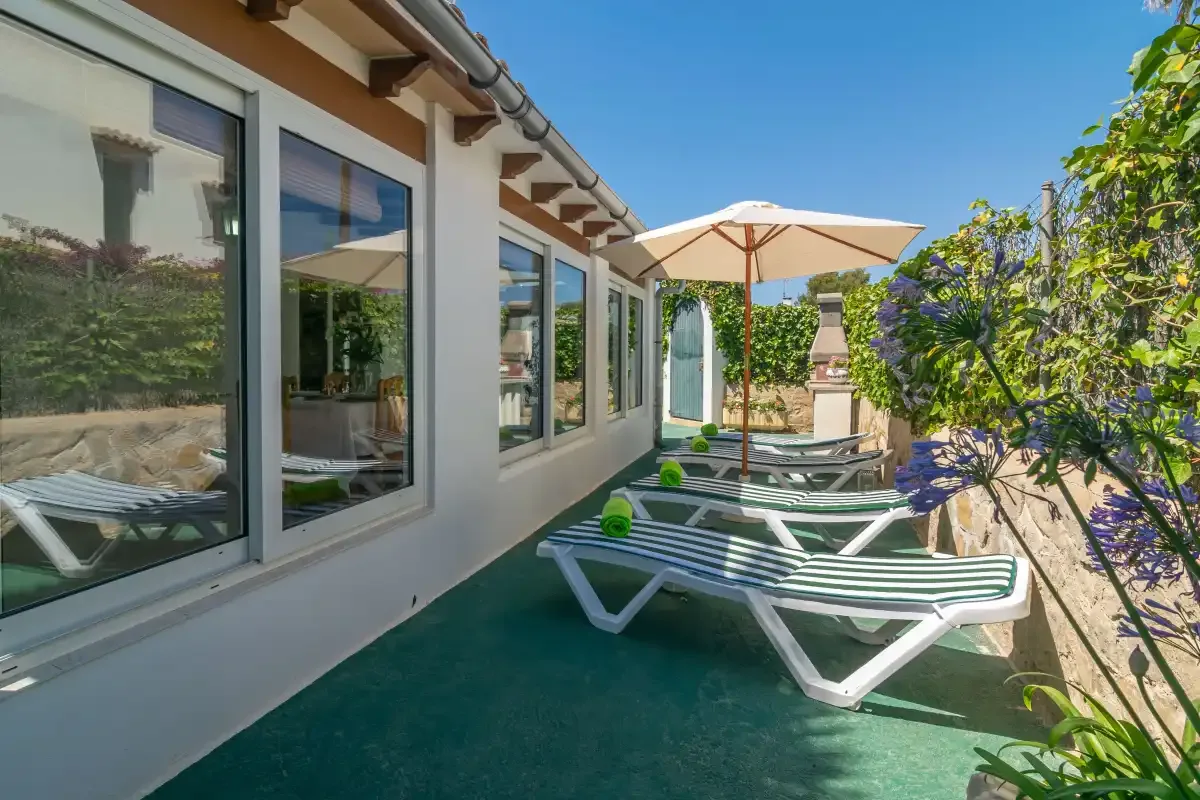 A sunny outdoor patio with lounge seating, an umbrella, and garden plants.