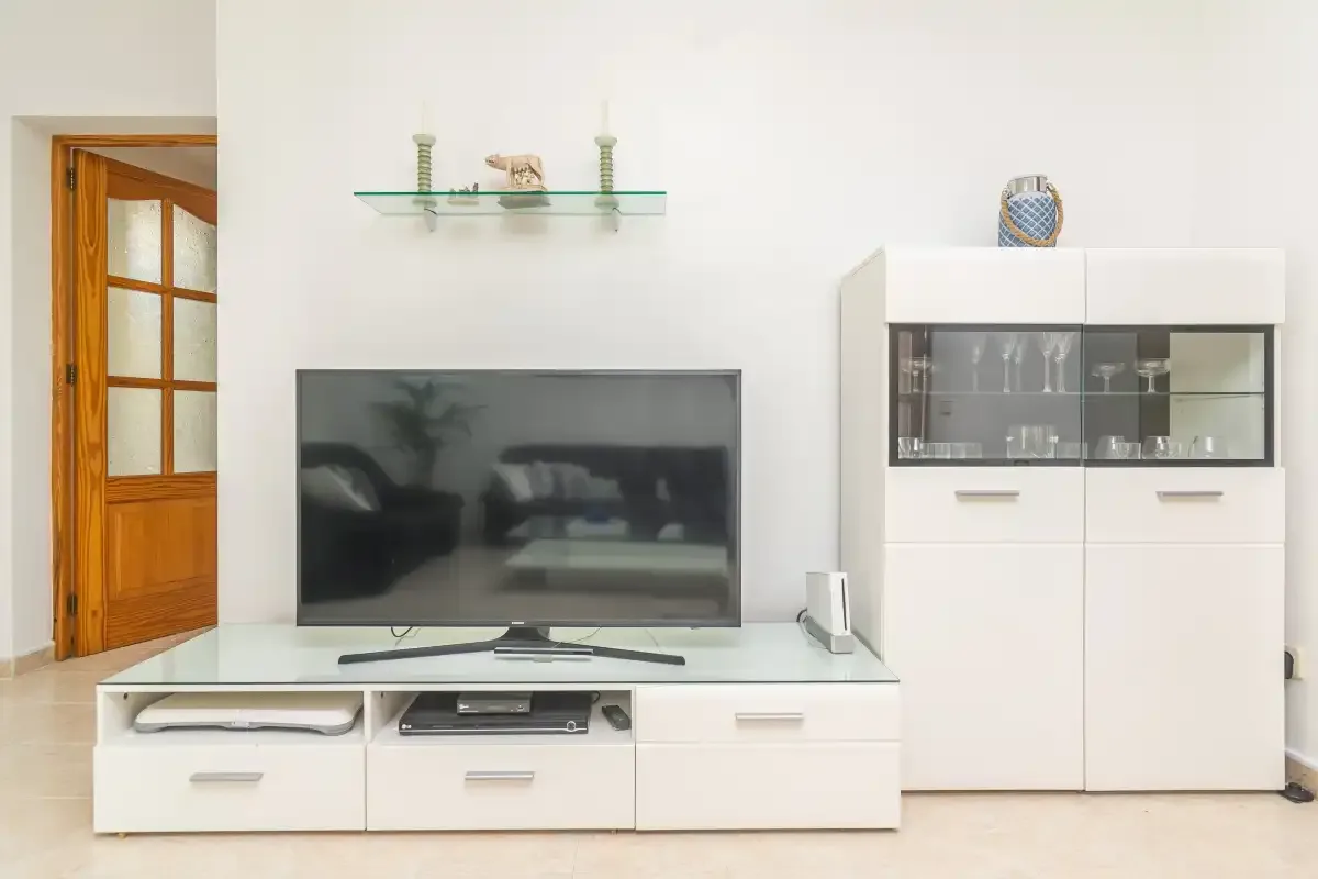 A living room features a television on a low cabinet beside a glass-fronted display cabinet.