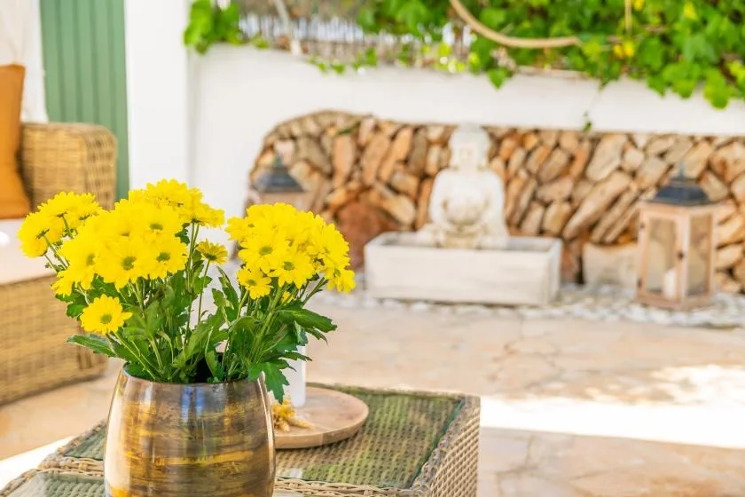 A patio seating area with a table of yellow flowers and a stone fountain.