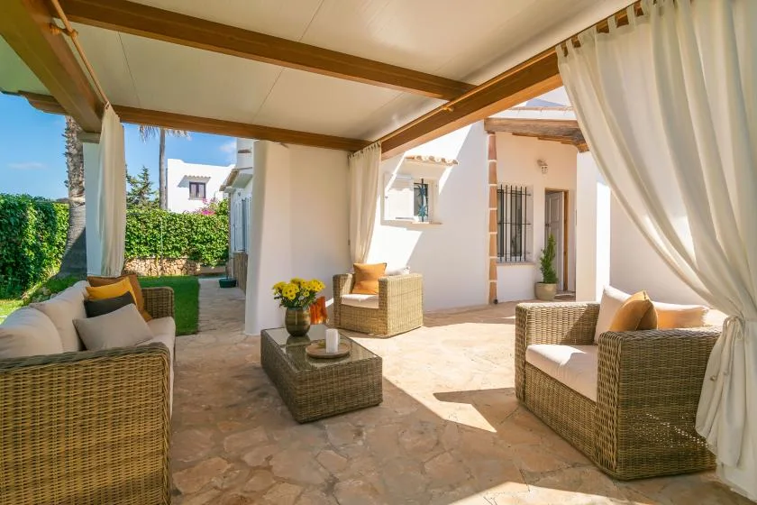 A covered patio with wicker seating and a low table opens onto a garden.