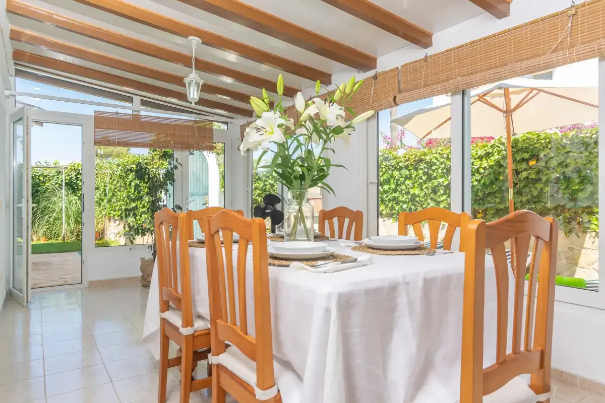 A bright dining area with a set table beside large windows overlooking greenery.
