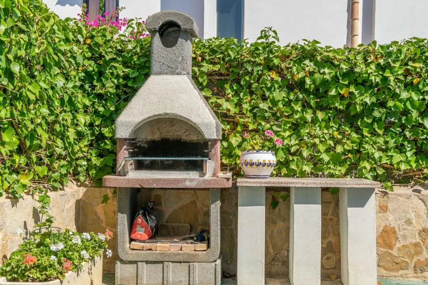 An outdoor barbecue grill stands beside a stone counter, with leafy greenery behind it.