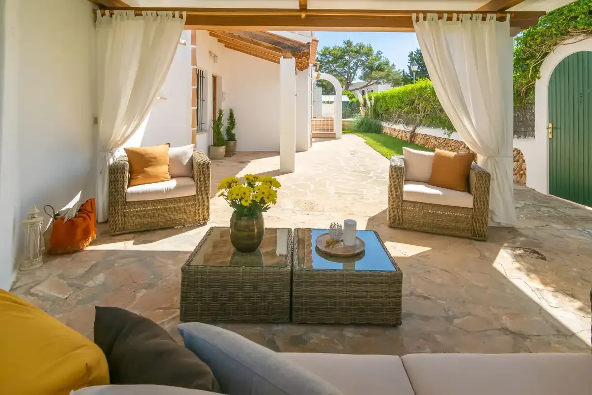 A covered patio with wicker seating and a coffee table opens onto a sunny courtyard.