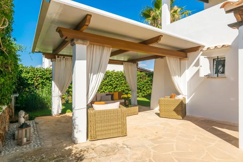 A covered outdoor seating area with wicker furniture and white curtains.