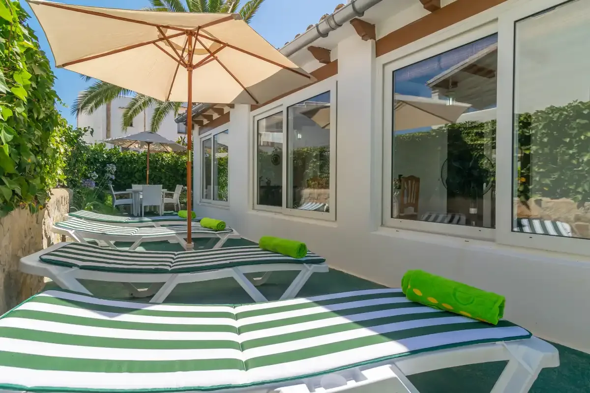 A sunny outdoor patio has striped lounge chairs beneath a large umbrella.