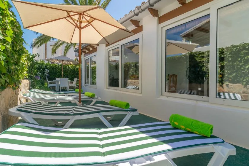 A sunny outdoor patio with striped loungers beneath a large umbrella.