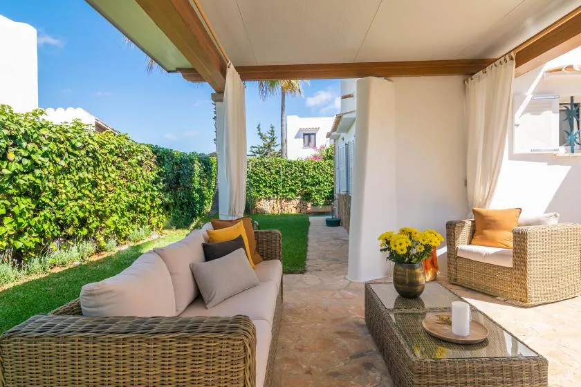 A covered outdoor seating area opens onto a small garden with leafy hedges.