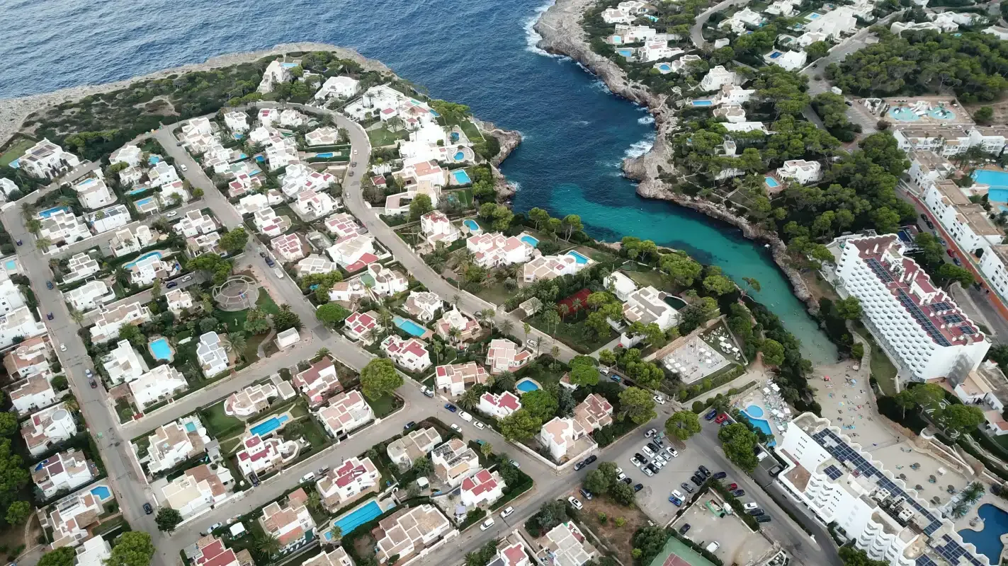 An aerial view shows coastal homes beside a narrow inlet and the sea.