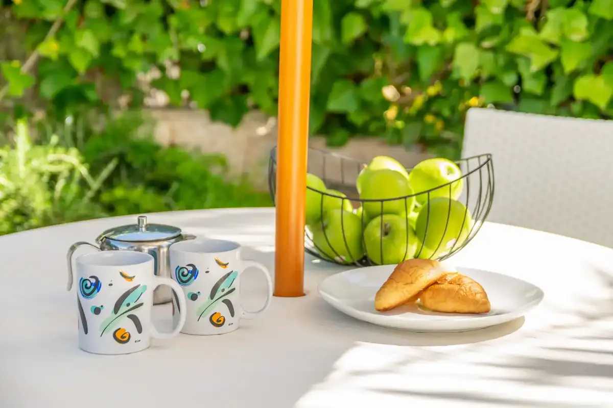 A garden table holds cups, fruit, and pastries.