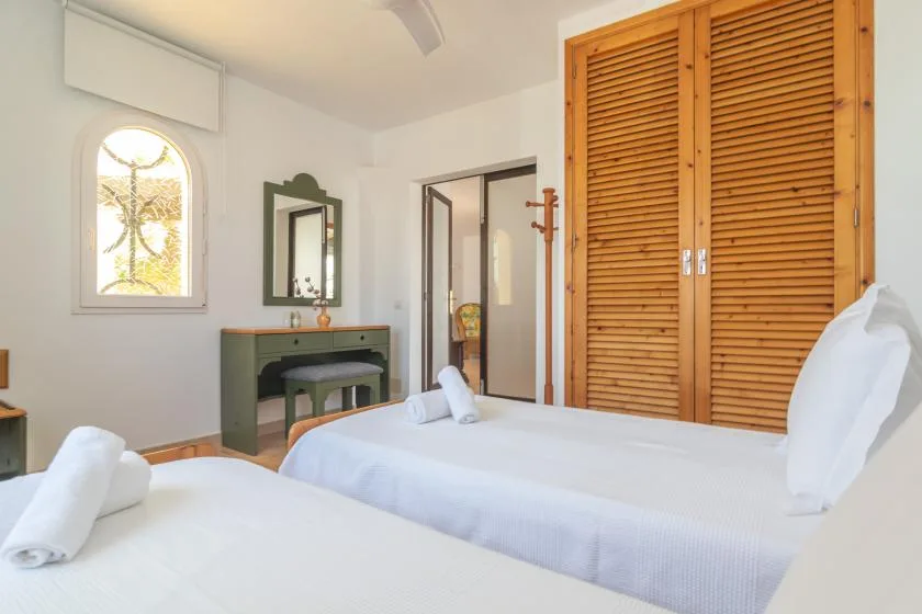 A bright bedroom with two beds, a vanity, and wooden louvered closet doors.