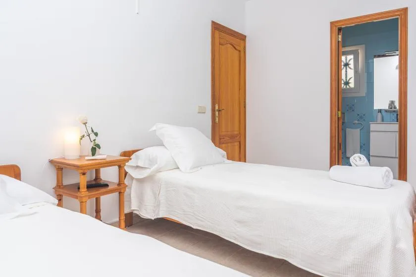 A bright bedroom with two beds and a wooden bedside table.