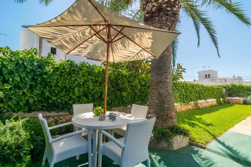 An outdoor dining area sits beneath a large umbrella beside a green lawn.