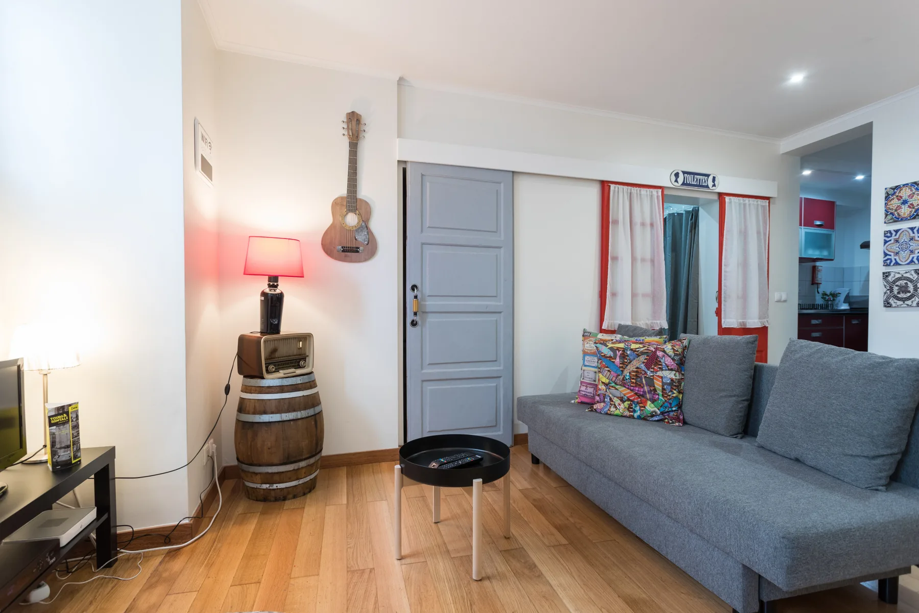 A living room with gray seating, a small coffee table, and a guitar on the wall.