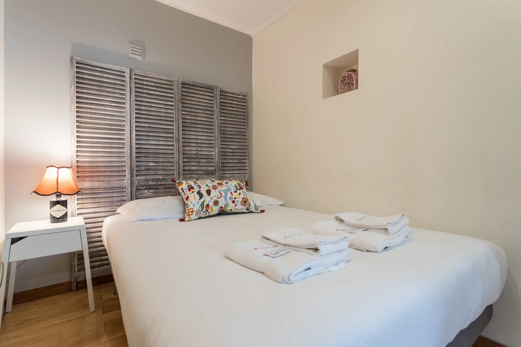 A bedroom with a neatly made bed and wooden shutters.