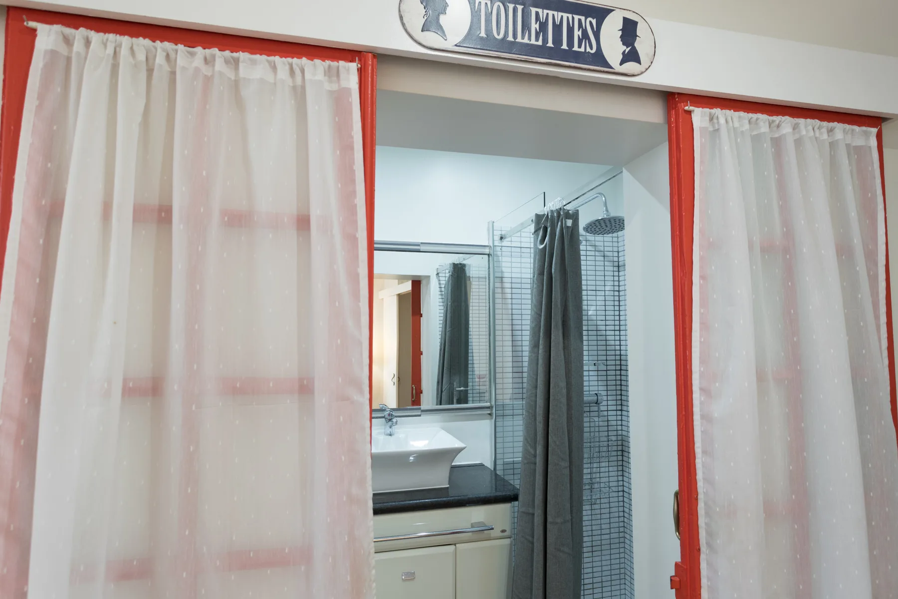 A bathroom with a sink and shower behind curtains.
