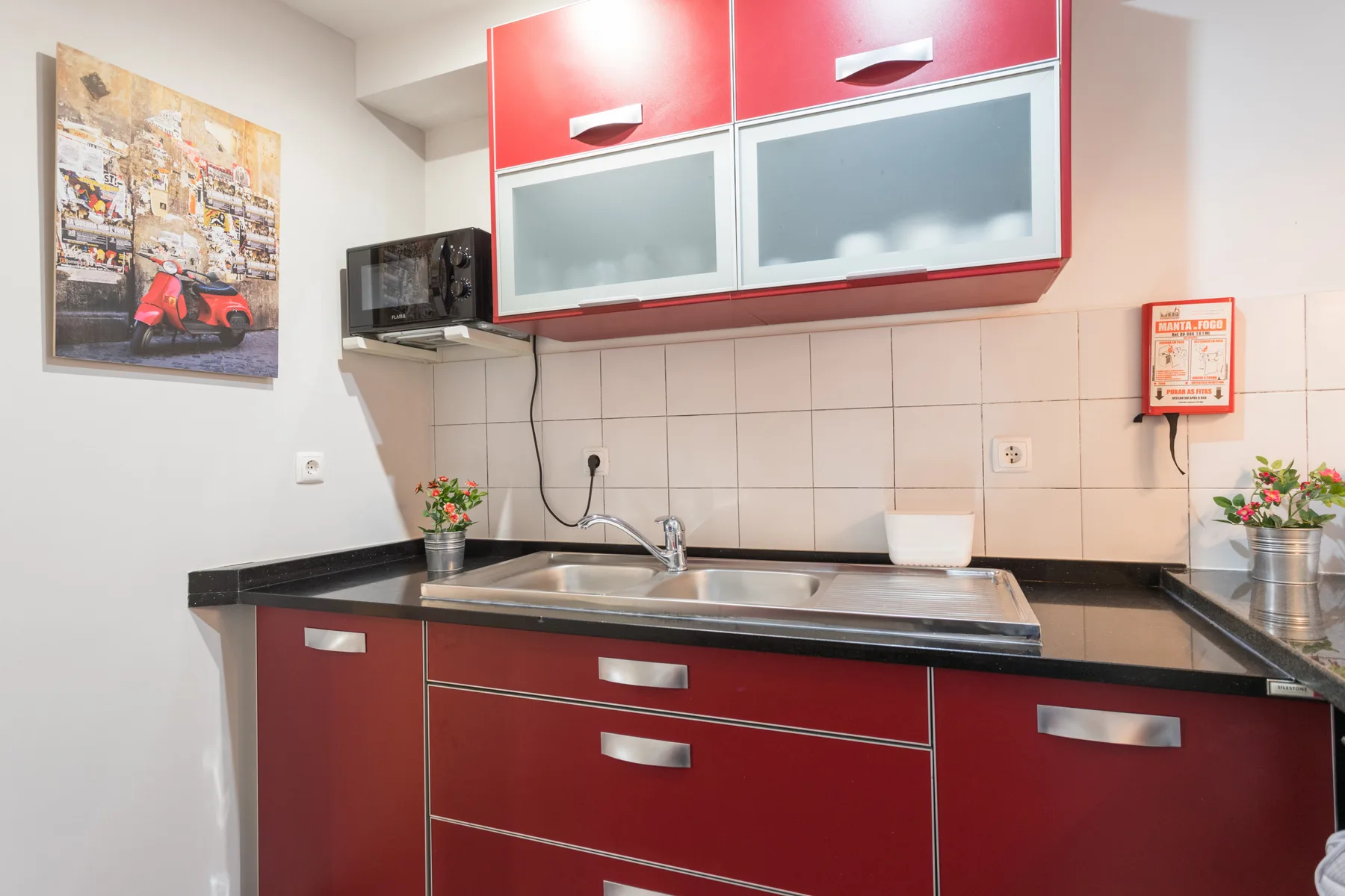 A compact kitchen with red cabinets, dark countertops, and a tiled backsplash.
