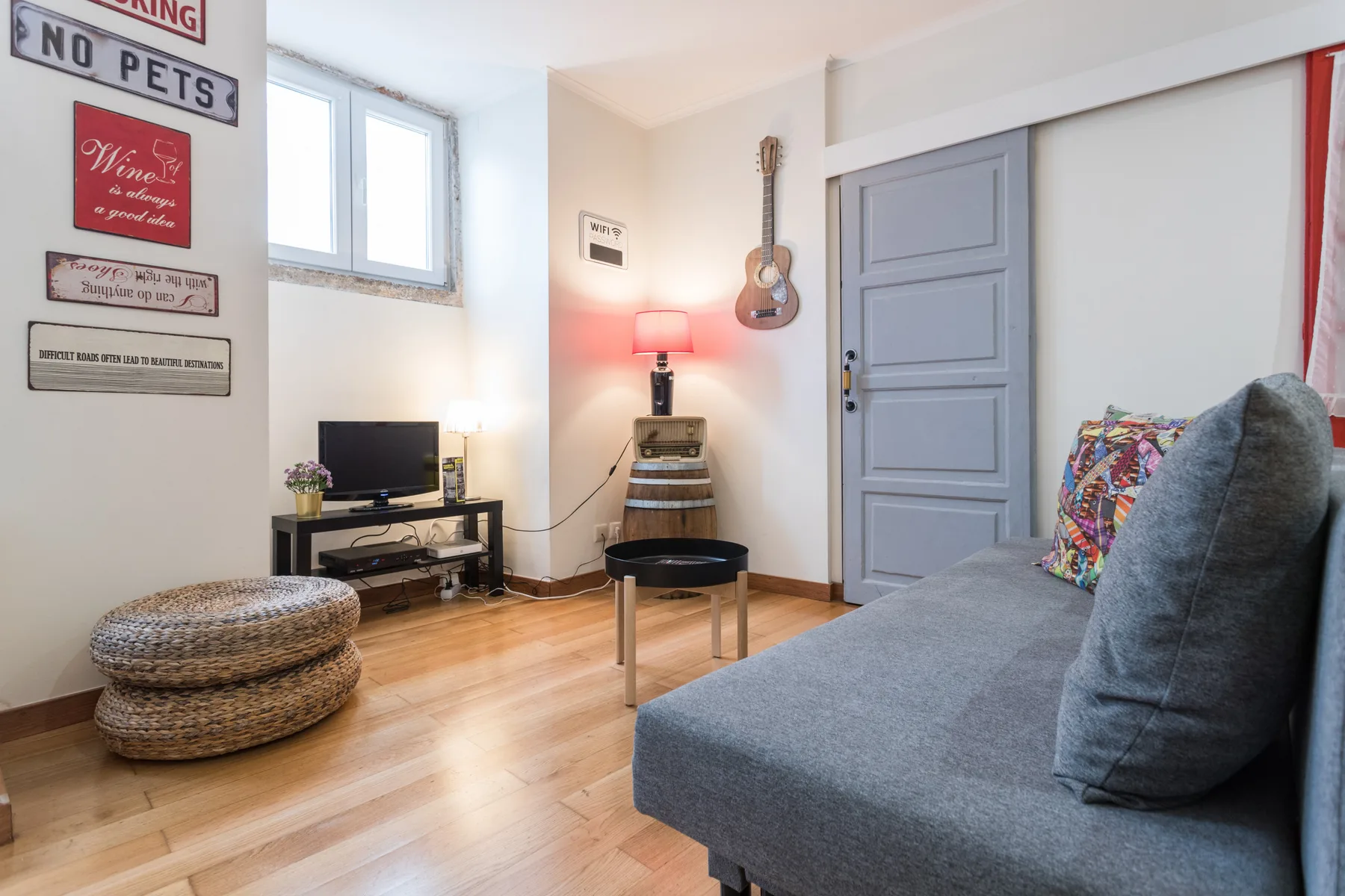 A living room with gray seating, a television, and a guitar on the wall.