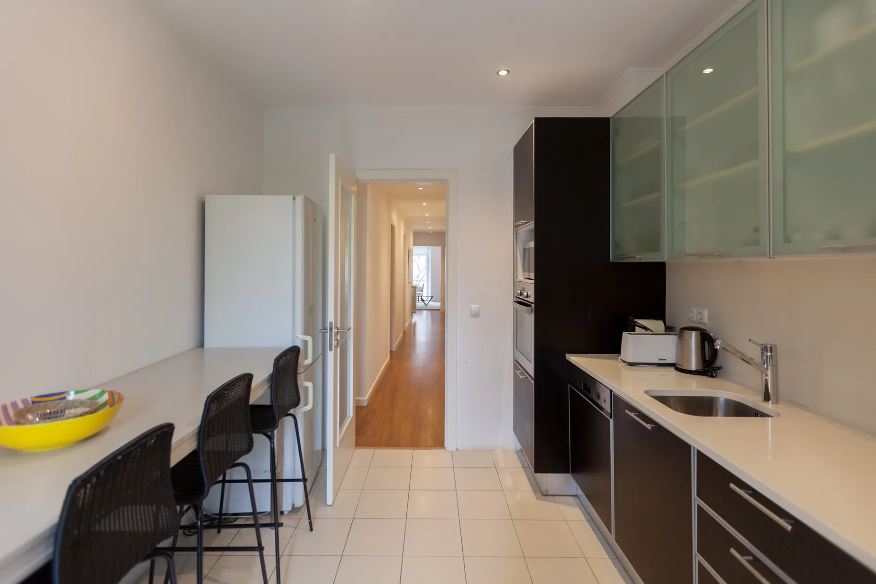 A narrow kitchen with a counter and a hallway leading to another room.